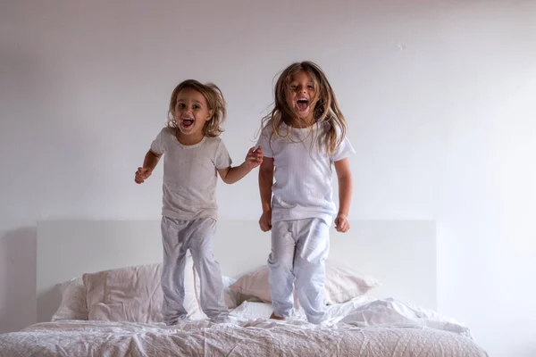 人の姉妹 白いパジャマを着てベッドにジャンプし 楽しい時を過します 幸福と自由の概念 — ストック写真