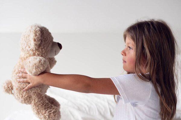 A little girl just wakes up in the morning, smiles, hugs her teddy bear and is happy about how she slept in her bed. Concept of: relax, love sleep and wake up in the morning