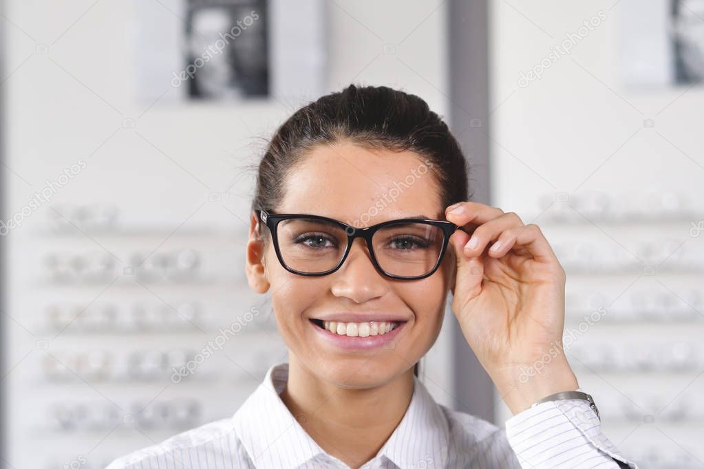 happy smiling woman in optical center adjusting eyewear glasses and looking at camera