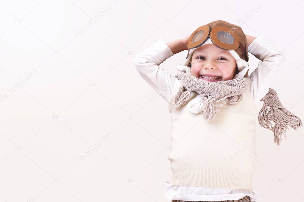 A girl in the bedroom dressed as an airman or a pilot pretends to drive a paper airplane isolated on a white background and imagines she is flying free in the sky. Concept of: freedom, success, dreams