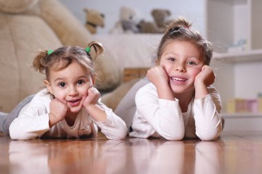 Arka planda gülümseyen doldurulmuş hayvanlar ve bebek evi kendi yatak odasında yerde yatan iki kız kardeş portresi. Kavramı: Aile, kız kardeşler, ev ve mutluluk