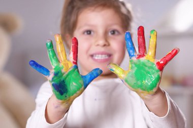 Ellerini tüm boya ile renkli gösterilen yatak odasında küçük bir kız portresi. Kavramı: renk, yaratıcılık, sanat, mutluluk ve eğitim.