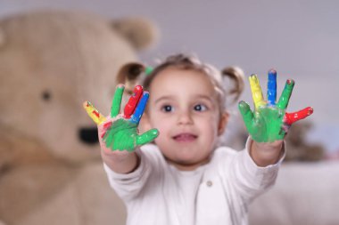 Ellerini tüm boya ile renkli gösterilen yatak odasında küçük bir kız portresi. Kavramı: renk, yaratıcılık, sanat, mutluluk ve eğitim.
