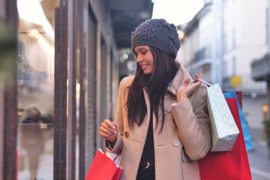 şehirde yürümek, alışveriş çantaları taşırken ve pencere ekrana bakarak şapkalı güzel esmer kadın 