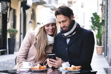 Bir barda açık havada otururken kahvaltı aşık bir çift var ve fotoğraflar arasında saygısız ve eski anıları kazma telefon bakmak. Kavramı: aşk, Sevgililer günü, teknoloji