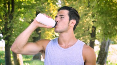 Portre yakışıklı genç sporcu içme suyu şişe yeşil park açık havada duran adam 