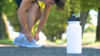 kısmi adam görünümünü bağlanacak üzerinde beyaz spor ayakkabı ayakkabı bağcığı, plastik şişe su ile yol 