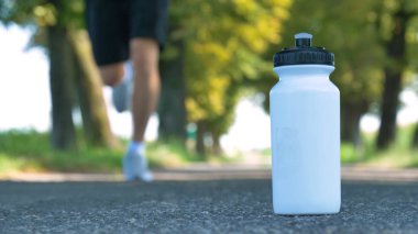 Açık havada, su şişesi asfalt yol üzerinde koşan atlet adam 