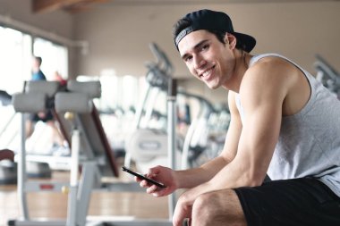 Bir egzersiz ve diğer arasında istirahat ederken bir spor salonunda bir adam portresi telefonunu sosyal ağlar izlemek veya iletileri göndermek için kullanır. Kavramı: spor, kişisel antrenör, iletileri, telefon