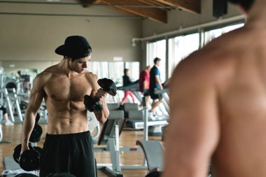 Salondaki, gömleksiz adam vücudu fit kalmak ve kasları tanımlamış olduğunuz için eğitiyor. Atlet ağır ağırlık ve yorgunluk yükseltir. Kavramı: spor, spor salonu, kas ve fitness