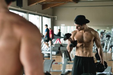 Salondaki, gömleksiz adam vücudu fit kalmak ve kasları tanımlamış olduğunuz için eğitiyor. Atlet ağır ağırlık ve yorgunluk yükseltir. Kavramı: spor, spor salonu, kas ve fitness