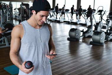 Bir egzersiz ve diğer arasında istirahat ederken bir spor salonunda bir adam portresi telefonunu sosyal ağlar izlemek veya iletileri göndermek için kullanır. Kavramı: spor, kişisel antrenör, iletileri, telefon