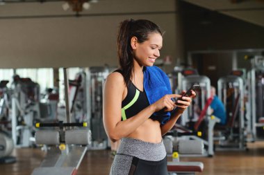 Güzel bir genç kadın okuma sırasında bir ileti gülümsüyor ve spor salonunda müzik dinlemek.