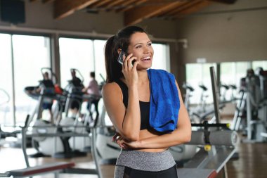 Güzel bir genç kadın okuma sırasında bir ileti gülümsüyor ve spor salonunda müzik dinlemek.