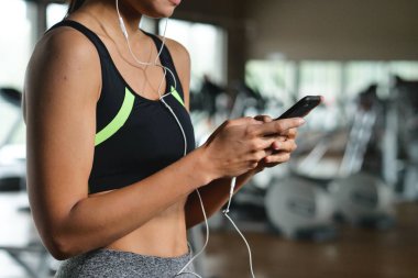 Güzel bir genç kadın okuma sırasında bir ileti gülümsüyor ve spor salonunda müzik dinlemek.