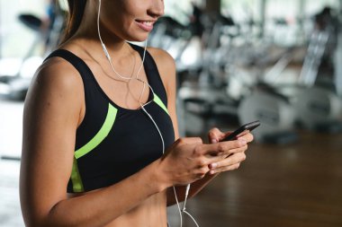 Güzel bir genç kadın okuma sırasında bir ileti gülümsüyor ve spor salonunda müzik dinlemek.