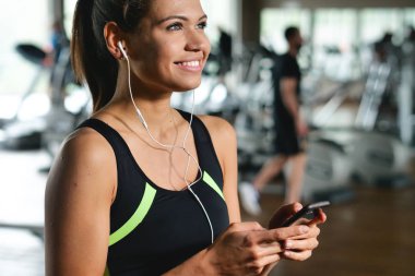 Güzel bir genç kadın okuma sırasında bir ileti gülümsüyor ve spor salonunda müzik dinlemek.