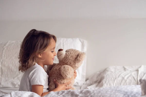 一个小女孩早上刚醒来 微笑着拥抱着她的泰迪熊 对自己睡在床上的方式很高兴 爱睡觉 早上醒来 — 图库照片