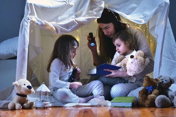 一位母亲带着女儿在卧室里玩耍 在用床单建造的帐篷里读童话故事 — 图库照片