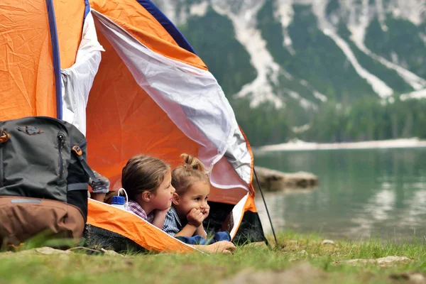 Two sisters camping at the lake, they enjoy playing in the tent, surrounded by nature. Concept of: sisterhood, travel, camping for children.