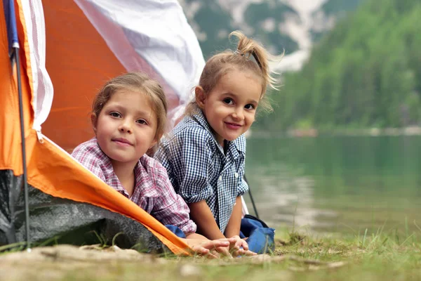 Two sisters camping at the lake, they enjoy playing in the tent, surrounded by nature. Concept of: sisterhood, travel, camping for children.