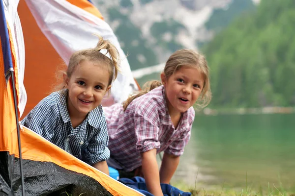 Two sisters camping at the lake, they enjoy playing in the tent, surrounded by nature. Concept of: sisterhood, travel, camping for children.