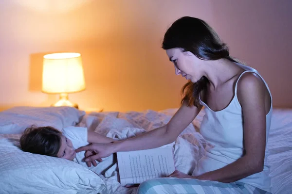 Mom reads a fairy tale of fantasy to her daughter in bed to make her fall asleep and let him have quiet dreams. Concept of: fantasy, relaxation, education, books.