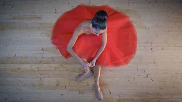 Portrait of a beautiful light ballerina, in a lush red dress, sits on a wooden floor, flexible, top view. Concept ballet dancer, slim diet light women, beautiful figure, healthy lifestyle, flexibility