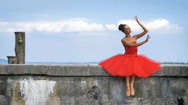 一个美丽的浅色芭蕾演员的肖像 穿着郁郁葱葱的红色礼服 坐在一个石墩上 芭蕾舞演员 轻盈的女人 柔韧性 美丽的身材 健康的生活方式 — 图库照片