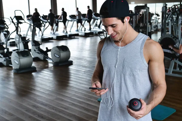 Bir egzersiz ve diğer arasında istirahat ederken bir spor salonunda bir adam portresi telefonunu sosyal ağlar izlemek veya iletileri göndermek için kullanır. Kavramı: spor, kişisel antrenör, iletileri, telefon