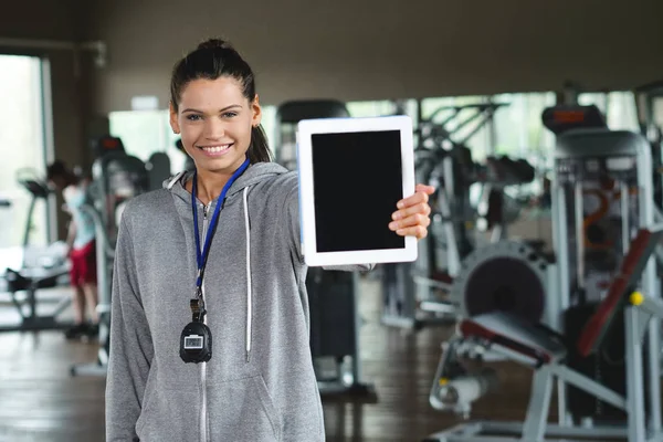 A woman personal trainer shows her tablet with her athlete\'s table and the type of training she has to do. Concept of: gym, personal trainer, training, technology.