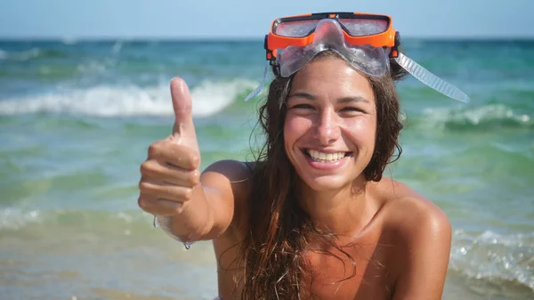 Beautiful young woman smiles at the sea, happy in a swimsuit wearing a diving mask.