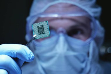Ultra Modern elektronik imalat fabrikası tasarım mühendisi olarak steril Coverall tutan mikro yongasında fütüristik holografi, Internet cyber security sembolleri ile.