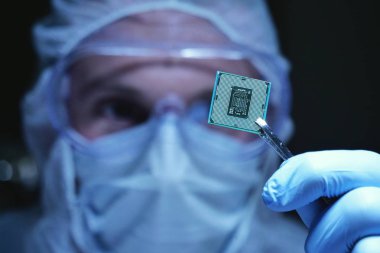 Ultra Modern elektronik imalat fabrikası tasarım mühendisi olarak steril Coverall tutan mikro yongasında fütüristik holografi, Internet cyber security sembolleri ile.