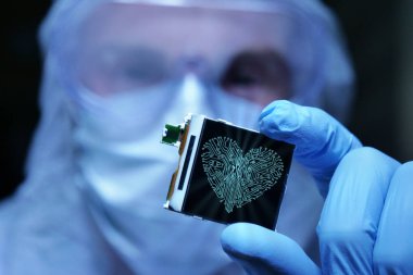 Ultra Modern elektronik imalat fabrikası tasarım mühendisi olarak steril Coverall tutan mikro yongasında fütüristik holografi sembolleri ile. aşk için bilgisayar.