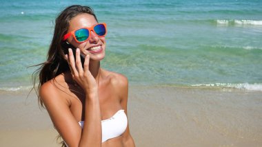 cep telefonu üzerinde konuşurken ve kumsalda ayakta gülümseyen güzel kadın  