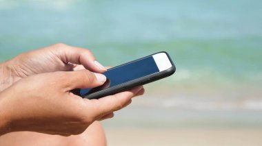 kız bir telefon tutarak denizin mavi deniz suyu arka plan üzerinde mesaj yazmak.