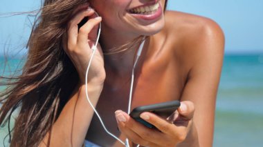 Güzel kız mutlu gülüyor ve deniz mavi su arka plan beyaz bir mayo içinde denizde telefonda müzik dinler.