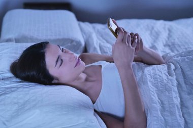 yatakta yatan ve akıllı telefon mesajlaşma esmer kadın 