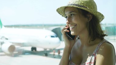 Onun uçuş için telefon, bir elbise, hasır şapka, gülümseyen, uçak konuşma bekleyen bir genç turist kız havaalanında, portresi. Konsept: dünyayı, tatil, tatil.