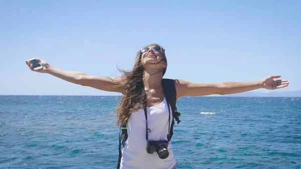観光写真家女性は携帯電話を保持して 彼女の背中に青い海と空の素晴らしい景色はバックパックを自由と感じ コンセプト 電話通信 — ストック写真