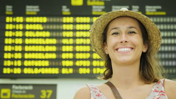 ドレスを着て 麦わら帽子身に着けているフライト スケジュールを見て 空港で美しい若い女の子の笑顔 世界旅行 リラックスのツアーのコンセプトは 飛行機のスケジュール — ストック写真