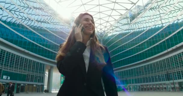 ガラス張りのモダンな建物で屋外携帯電話で話している完全なスーツでビジネスの女性のビデオ — ストック動画