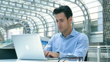 Gözlük, gülümseyen genç yakışıklı işadamı (öğrenci) ile bir dizüstü bilgisayar, çalışma masasında mavi gömlekli. Konsept: yeni iş, iş ilişkileri, kariyer büyüme, başarı, iş online.