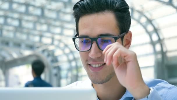 年轻的英俊商人 穿着一件蓝色衬衫 在桌子上与笔记本电脑一起工作 戴着眼镜 面带微笑 新业务 业务关系 职业发展 在线工作 — 图库视频影像