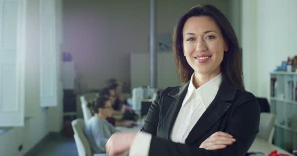 慢动作视频成功的微笑的女商人摆在相机上双臂交叉 而站在办公室与同事在后台 — 图库视频影像