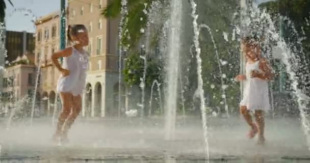 Дві Маленькі Дівчата Розважаються Грають Фонтані Посміхаючись Білих Сукнях Фоні — стокове відео