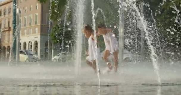 Две Маленькие Девочки Веселятся Играют Фонтане Улыбаясь Белых Платьях Фоне — стоковое видео