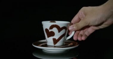Süper ağır çekim natürmort genç adam el 4 k siyah bir zemin üzerine izole kalp tasarımı ile beyaz porselen mug içinde küçük metal kaşık kakao ile karıştırma (yakın)