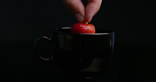 超级慢动作仍然生活的年轻人手滴下草莓在热巧克力倒在一个黑色瓷杯孤立的黑色背景在 宏观关闭 — 图库视频影像